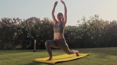 Spor kıyafetli kadın dışarıda yoga pozu veriyor. Parkta esneme hareketleri yapan atletik kız. Spor salonundaki kadın yeşil çimenler üzerinde yoga egzersizleri yapıyor. Açık havada spor yapan bir kız. Yavaş çekim