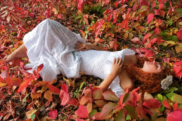 Red-haired young woman lying among red leaves — Stock Photo, Image