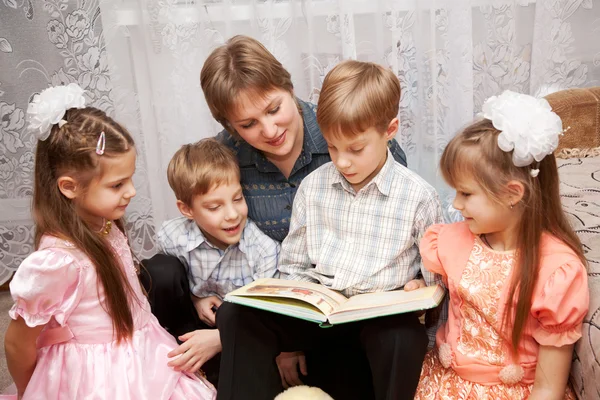 Mère heureuse et quatre enfants lisant un livre . — Photo