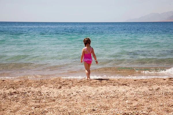 Liten flicka stående på stranden i baddräkt. bakifrån. — Stockfoto