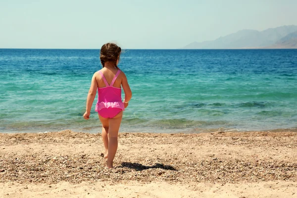 Little girl standing on beach in swimsuit and going to swim — Stock Photo, Image