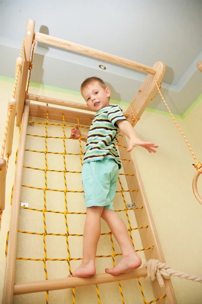 Ein kleines Kind klettert auf einem Seilnetz. von unten. — Stockfoto