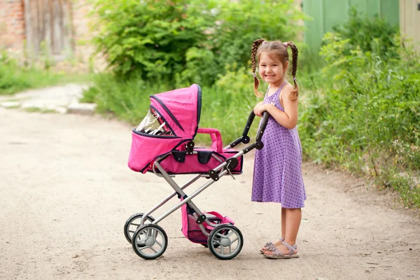 Niña caminando con carrito de juguete. Pequeña mamá . — Foto de Stock