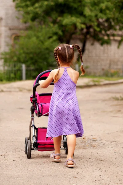 Menina caminhando com carrinho de brinquedo. Pequena mamã . — Fotografia de Stock