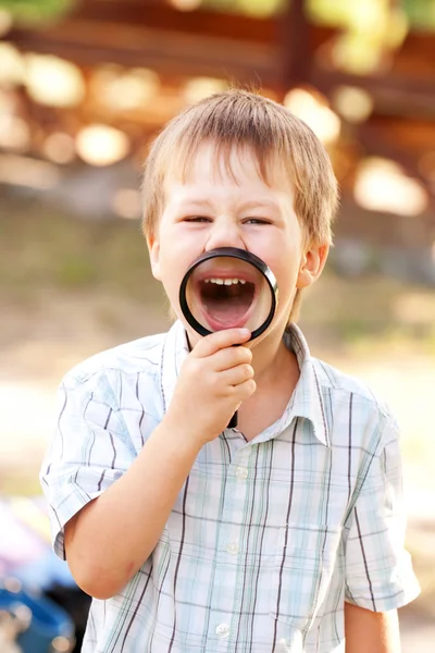 Маленький хлопчик посміхається через збільшувальне скло — стокове фото