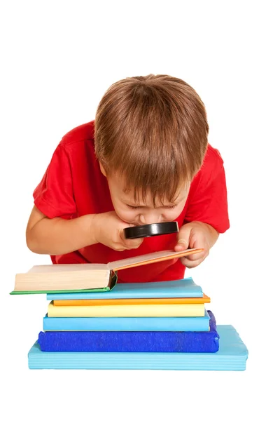 Niño pequeño con gafas leyendo un libro con una lupa — Foto de Stock