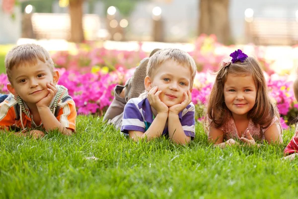 Trzy szczęśliwe dzieci leżąc na trawie — Zdjęcie stockowe