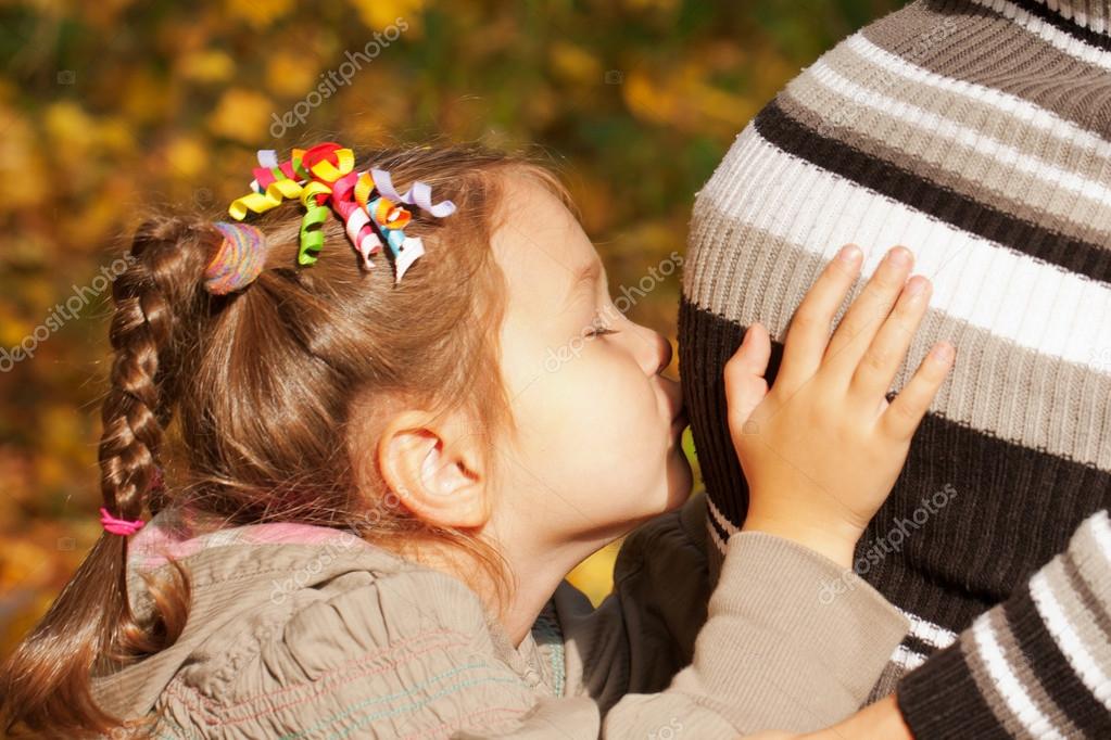 Little girl hugging and kissing her mother's pregnant belly, ready for your logo, text or symbols