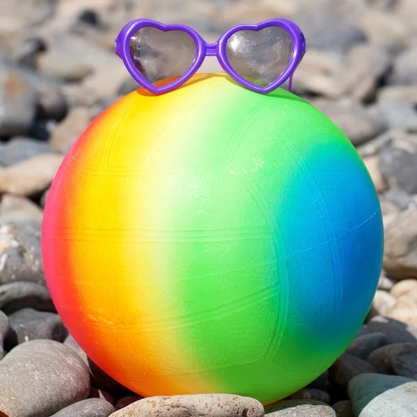 Colorful beach ball with sunglasses on the pebbles. — Stock Photo, Image