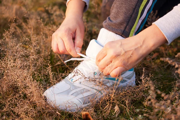 Las manos de las mujeres atando los cordones en los zapatos deportivos — Foto de Stock