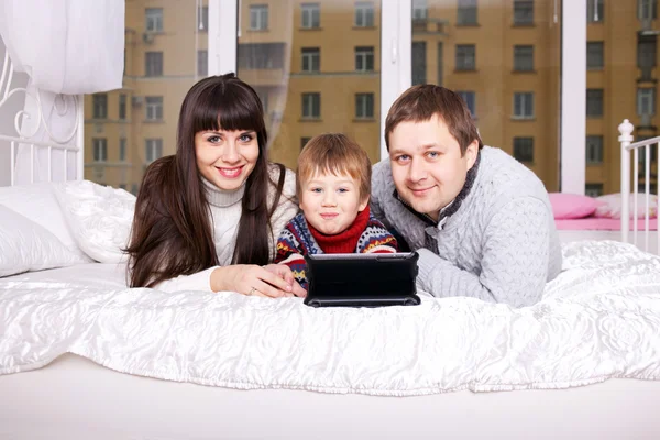 Lycklig familj med tabletten liggande på sängen. — Stockfoto