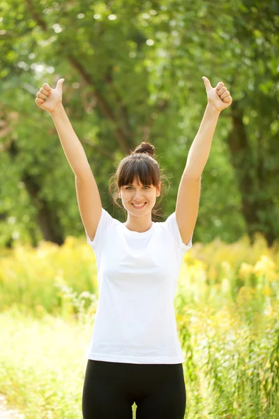 Woman in white t-shirt showing a thumbs up sign outdoors. Ready — Stock Photo, Image