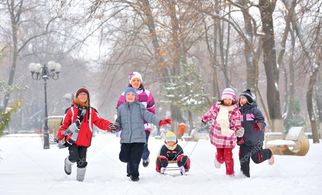 Group of children and mother playing on snow in winter time