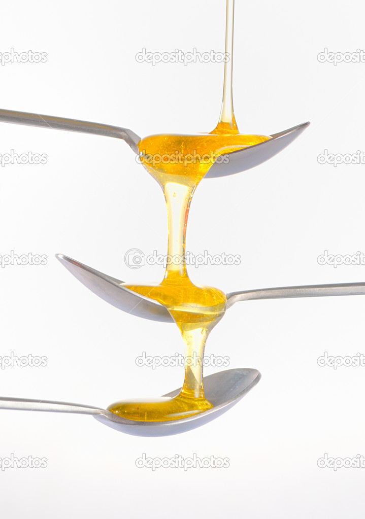 Honey dripping over three silver teaspoonful 
