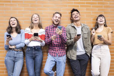 Bir grup mutlu arkadaş dışarıda cep telefonlarıyla eğleniyor - gençler üniversitenin arka bahçesinde birlikte gülüyorlar - yüzlere odaklanın