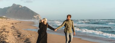 Sonbahar sezonu boyunca, gün batımında çöl sahilinde birlikte yürüyen hippi ve aşık genç çiftin olduğu yatay bir pankart.