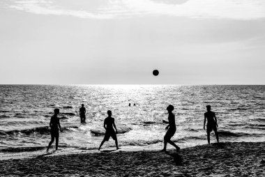 Gün batımında sahilde futbol oynayan mutlu arkadaşlar yaz tatilinde plaj futbolu oynayan genç arkadaşlarının siluetleri gün batımında arka planda tanınmayan gerçek insanlar.