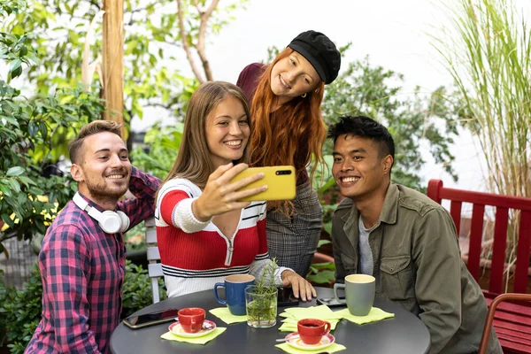 Çok kültürlü mutlu arkadaşlar kahve molası sırasında bahçede grup fotoğrafı çektirip eğleniyorlar. - Melez ırk gençleri birlikte gülüyor ve tatilde eğleniyorlar.