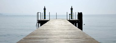 Mavi gökyüzü üzerinde ahşap iskele ile yatay bayrak ya da başlık Sabah sakin bir rıhtım - Bardolino, İtalya