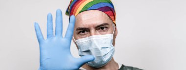 Başında mavi eldivenle elini gösteren koruyucu maskeli ve gökkuşağı bantlı cerrah doktorla yatay pankart veya başlık - Doktor HIV virüsünü veya koronavirüsü önleme ile durduruyor