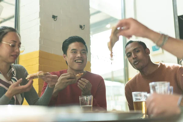 在现代比萨饼店餐厅吃比萨饼的朋友们笑笑 与多种族人士的友谊概念 与比萨饼和啤酒品脱一起享受在比萨饼店的快乐时光 — 图库照片