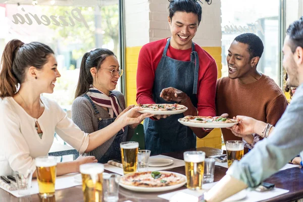在舒适的比萨饼店餐厅里 自信的侍者为多文化的朋友提供美味的比萨饼 多民族的朋友在比萨饼店一起吃比萨饼 喝金发啤酒 — 图库照片