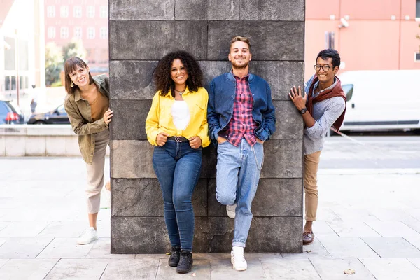 Üniversite kampüsündeki duvarda eğlenen çok ırklı arkadaş grubu, şehrin dışında kutlama yapan çeşitli kültür öğrencileri, grup fotoğrafı için kameraya bakan gülümseyen genç insanlar.