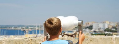 Tanımlanamayan sarışın çocukla yatay bayrak ya da başlık yukarıdan halka açık dürbünlerden denize bakıyor