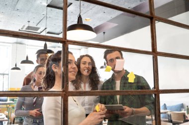 Duvardaki cam ofis hakkında kağıt not yazma stratejisi ile fikir paylaşımı - genç iş adamları ve kadınların ofiste buluşması ve fikir paylaşımı için post it notları - beyin fırtınası konsepti