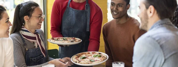 在舒适的比萨饼店餐厅里 有知己的侍者为多文化的朋友提供美味的比萨饼 多民族朋友一起吃比萨饼很开心 — 图库照片