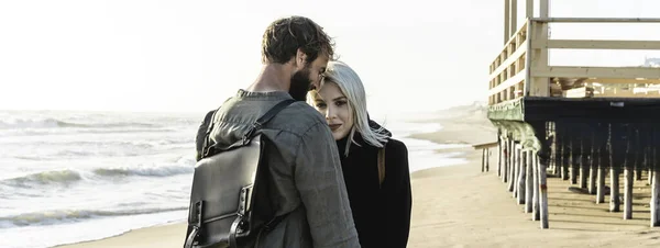 Ahşap yapının yakınındaki vahşi sahilde birbirine aşık romantik hipster çiftlerle yatay pankart ya da başlık - erkek arkadaş ve kız arkadaş havalı kıyafetler ve klasik sırt çantası giyerek