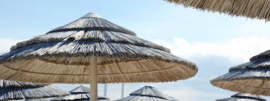 Güneşli bir günde denize yakın tropik bir sahilde mavi bir gökyüzüne karşı saman şemsiyeli yatay pankart ya da başlık. Lüks tatil konsepti. Metin için alanı kopyala