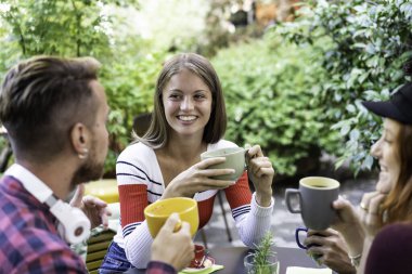 Arkadaş grubu kafeteryada cappuccino içiyor - insanlar kafeterya bahçesinde sohbet ediyor ve eğleniyorlar - restoranda mutlu erkekler ve kızlarla arkadaşlık konsepti - kadın yüzüne odaklan