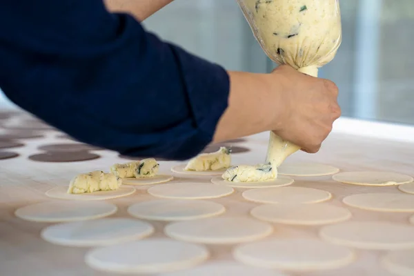 Woman prepare fresh made ravioli inside pasta factory. Using a pastry bag or sac a poche to make stuffed pasta ravioli, culurgiones, agnolotti. Focus on stuffed