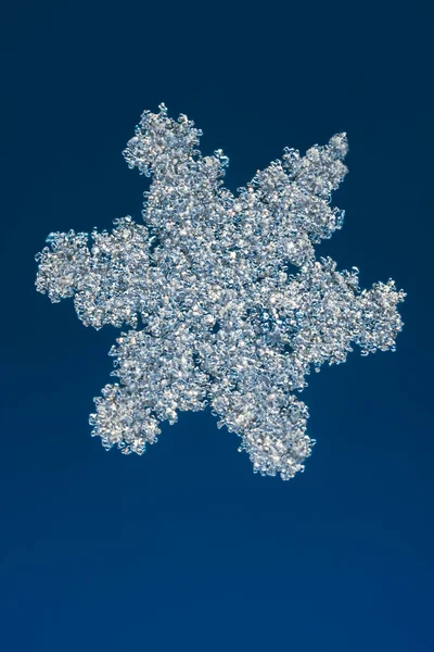 Echte sneeuwvlok bij hoge vergroting. Macro foto van kleine sneeuw bubbels kristal, sneeuwvlok gloeien op donkerblauwe achtergrond — Stockfoto