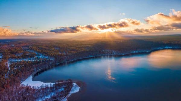 Вид с воздуха на зимний фон с заснеженным лесом, озером и солнечными лучами над озером Глукас в Литве — стоковое фото