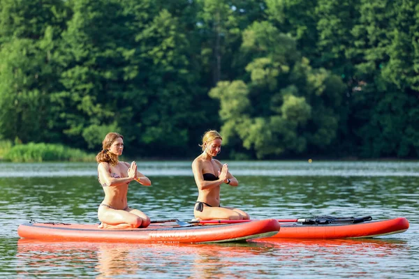 Deux jeunes femmes faisant du yoga ensemble sur la planche au milieu du lac — Photo