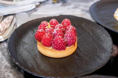 Servis masasında siyah tabakta ahududulu tart.