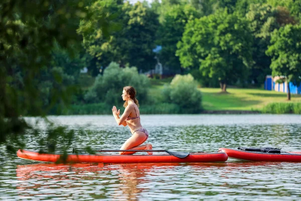 Mladá žena dělá jógu na prkně uprostřed jezera — Stock fotografie