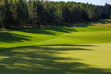  Manzara, golf sahası, arka planda yeşil çimenler ve bulutlu parlak bir gökyüzü.