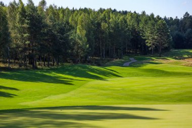  Manzara, golf sahası, arka planda yeşil çimenler ve bulutlu parlak bir gökyüzü.