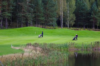 Golf sahası, manzara, arka planda yeşil çimenler ve bulutlu parlak bir gökyüzü.