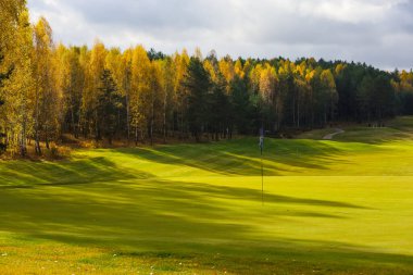 Sonbahar golf sahası, manzara, arka planda yeşil çimenler ve bulutlu parlak bir gökyüzü.