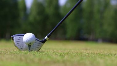 Close-up of a golfers hand putting the ball on a stand, putter on the background