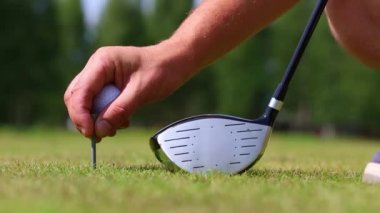 White golf ball on a stand on a green field, putter on the background