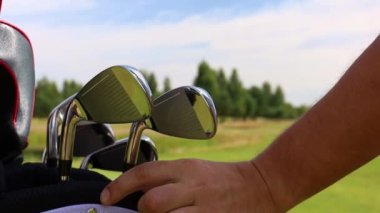 Adam gardırop bagajından golf sopasını alıp topa vurmaya hazırlanıyor.