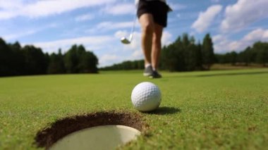Top deliğe yuvarlanıyor, adam golf oynuyor.