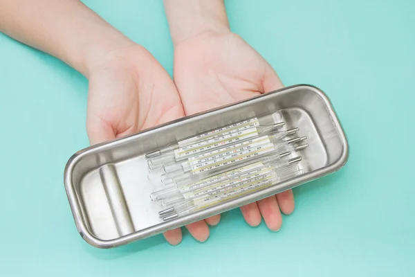 Hand with pile of medical thermometer in tray — Stock Photo, Image