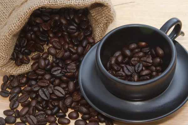 Grão de café em xícara de café preto — Fotografia de Stock