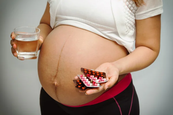 Ventre de la femme enceinte et des pilules vitaminiques et un verre d'eau dans — Photo